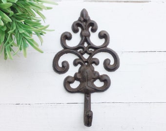 May include: A black cast iron wall hook with a decorative, ornate design. The hook is shaped like a stylized leaf with a single hook at the bottom.
