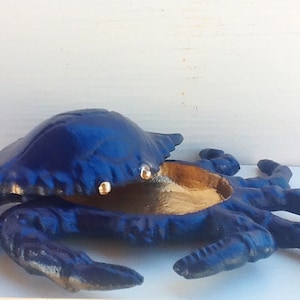 May include: A blue cast iron crab shaped trinket box with a gold interior. The box is open and the lid is propped up.