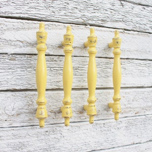 May include: Four yellow painted cabinet knobs with a distressed finish. The knobs are attached to a white wooden surface.