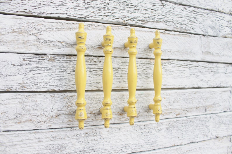 May include: Four yellow painted cabinet knobs with a distressed finish. The knobs are attached to a white wooden surface.