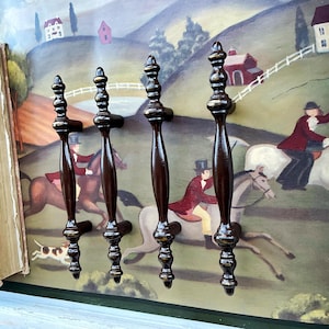 May include: Four brown metal cabinet knobs with a gold finish and a decorative design. The knobs are arranged in a row against a background of a painting.