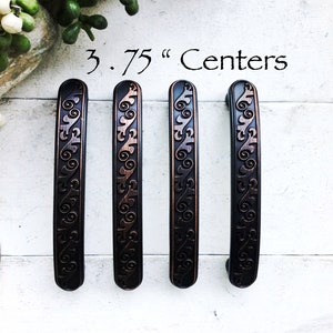 May include: Four ornate, black cabinet pulls with a copper finish and a decorative scroll design. The pulls are 3.75 inches apart.