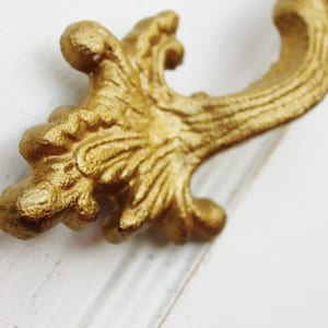 May include: A gold-colored ornate metal drawer pull with a decorative, scroll-like design.