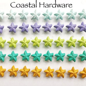 May include: A set of 30 starfish drawer pulls in five different colors: light blue, purple, green, teal, and yellow. The starfish are arranged in rows on a white surface. Coastal Hardware.