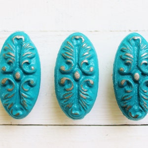 May include: Three turquoise blue oval-shaped cabinet knobs with a gold-colored ornate design.