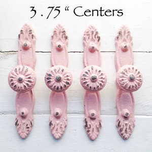 May include: Four pink metal cabinet knobs with a decorative floral design and a 3.75 inch center to center spacing.