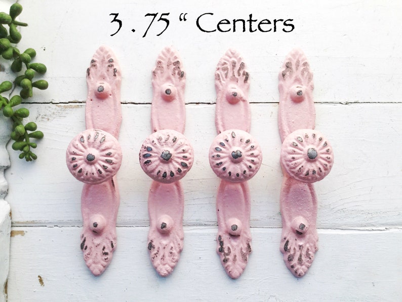 K&ouml;nnte beinhalten: Vier rosafarbene Metall-Schrankkn&ouml;pfe mit einem dekorativen Blumenmuster und einem Abstand von 9,5 cm von Mitte zu Mitte.