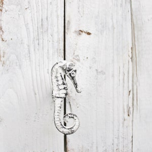 May include: White painted metal seahorse door knob or pull. The seahorse is in a curled position with its tail curled around its body.