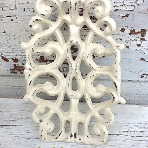 May include: A white, ornate, cast iron decorative piece with a distressed finish. The piece has a delicate, floral design and is reminiscent of a vintage style. The text "Shabby Cream" is visible at the bottom of the image.