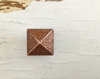May include: A square, copper-colored pyramid-shaped knob with a textured surface.
