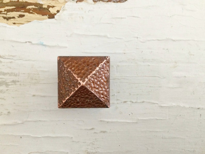 May include: A square, copper-colored pyramid-shaped knob with a textured surface.