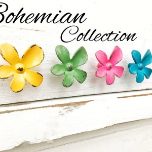 May include: Four flower-shaped cabinet knobs in yellow, green, pink, and blue. The knobs are arranged in a row on a white wooden surface. The text "Bohemian Collection" is written above the knobs.
