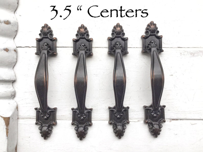 May include: Four antique-style cabinet pulls with a 3.5" center-to-center spacing. The pulls are made of a dark metal with a slightly aged finish.