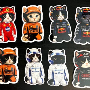 May include: A collection of ten stickers featuring cartoon cats dressed in Formula 1 racing attire. The cats wear helmets and racing suits in various team colors, including red, orange, black, and white. The stickers have a white border.