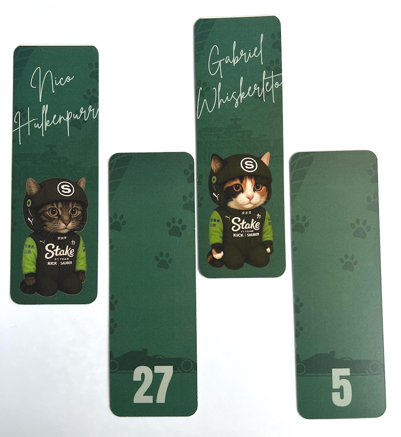 May include: Green rectangular bookmarks featuring cartoon cats in racing attire. One bookmark has the name "Nico Hulkenpurr", another "Gabriel Whiskerto". The other two bookmarks have the numbers 27 and 5. The bookmarks have paw prints.