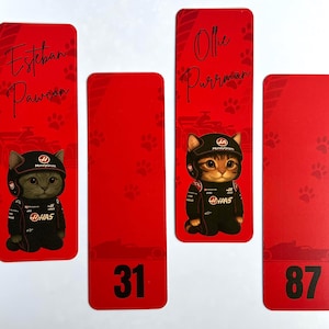 May include: Red bookmarks featuring a cartoon cat in a racing suit and helmet. The bookmarks have names like "Esteban Pawcon" and "Ollie Purrman", along with the numbers 31 and 87. Paw prints and race car silhouettes decorate the background.