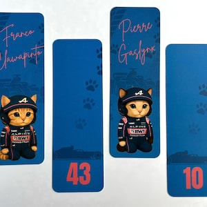 May include: Four blue bookmarks featuring a cartoon cat in a racing suit and helmet. The bookmarks have names and numbers: "Franco Clawapinto", "43", "Pierre Gaslynk", and "10". Paw prints and race car silhouettes decorate the background.