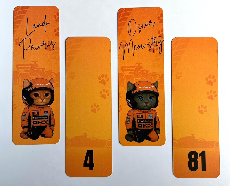 May include: Orange and yellow bookmarks featuring cartoon cats in racing suits and helmets. The bookmarks have the names "Lando Pawris" and "Oscar Meowstry" written on them, along with the numbers "4" and "81".