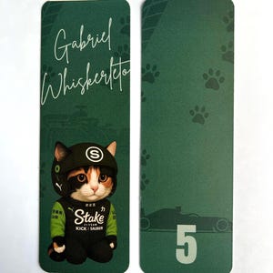 May include: Two green bookmarks. One features a cat wearing a racing suit and helmet with the text "Gabriel Whiskerteto". The other has paw prints and a race car with the number 5.