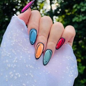 Pode incluir: Uma mão com unhas longas em forma de amêndoa, cada uma pintada com uma cor diferente e um contorno preto, lembrando o estilo de banda desenhada. As cores incluem azul, laranja, verde e vermelho, com um detalhe rosa e preto na unha mais longa.