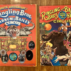May include: Two vintage Ringling Bros. and Barnum & Bailey Circus souvenir programs. The left cover is orange with a tiger and elephant graphic, celebrating the 100th anniversary. The right cover features a circus performer, an elephant, and a tiger.
