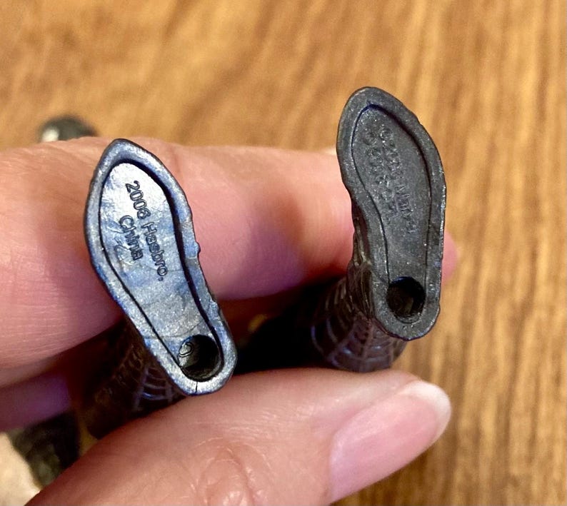 May include: Close-up of the feet of a black action figure. The soles of the feet are visible, with the text "2008 Hasbro China" imprinted on one foot. The other foot has a similar imprint. The figure is held by a person.