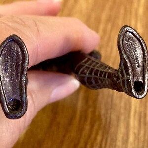 May include: A close-up of the feet of a Spider-Man action figure. The figure's feet are dark brown with a textured surface and a hole at the heel. The soles have imprinted text.