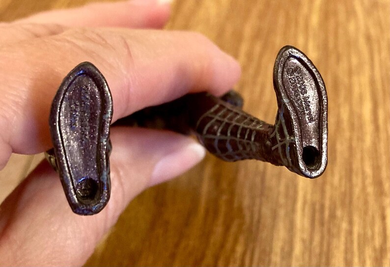 May include: A close-up of the feet of a Spider-Man action figure. The figure's feet are dark brown with a textured surface and a hole at the heel. The soles have imprinted text.