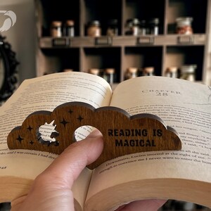 May include: A wooden bookmark shaped like a cloud with a unicorn cutout. The bookmark has the text "Reading is Magical" engraved on it.