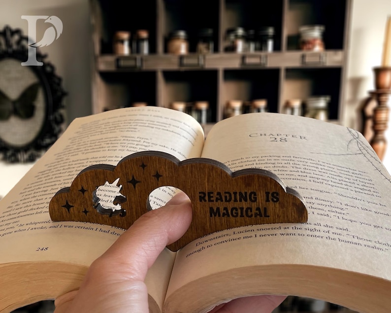 May include: A wooden bookmark shaped like a cloud with a unicorn cutout. The bookmark has the text "Reading is Magical" engraved on it.