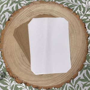 May include: A white, rectangular, blank card with rounded corners is placed on a wooden surface with a floral pattern.