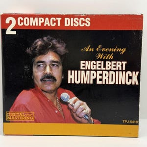 Könnte beinhalten: CD-Box mit einem Porträt von Engelbert Humperdinck. Die Box ist schwarz mit roten und gelben Akzenten. Der goldfarbene Schriftzug lautet "An Evening With Engelbert Humperdinck". Enthält 2 CDs.