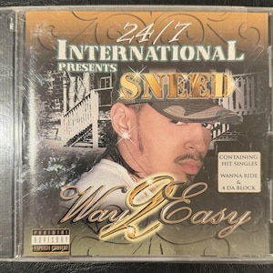 Może przedstawiać: Pudełko na płytę CD z albumem "Way 2 Easy" Sneed. Okładka przedstawia portret artysty w czapce moro. Tytuł albumu jest w złotym skrypcie, z tekstem "24/7 International Presents" na górze.
