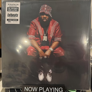 May include: A vinyl record album cover featuring Raekwon wearing a red leather jacket, matching shorts, and a patterned bucket hat. The cover includes a white sticker with the text Raekwon, The Emperor's New Clothes, and Fatbeats. A black stand displays the text NOW PLAYING.