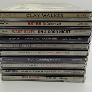 May include: A stack of compact disc albums featuring country music artists. Titles include Clay Walker, Tracy Byrd, Wade Hayes, Bonnie Raitt, Neal McCoy, and Alan Jackson. The album covers are visible, showcasing artist names and album titles.