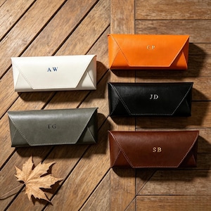 May include: Five rectangular, foldable spectacle cases in white, orange, black, olive green, and brown. Each case features a triangular front flap and is personalised with two-letter initials in gold or dark blue foil stamping on the front centre.