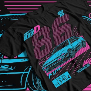 Può includere: T-shirt nero con grafica stilizzata di un'auto sportiva blu e il numero "86" in rosa. Il design include testo giapponese e una targa. La maglietta ha un'estetica retrò.