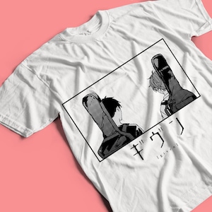 Puede incluir: Camiseta blanca con una ilustración en blanco y negro de estilo manga de dos figuras con fundas de guitarra. El diseño está enmarcado en un rectángulo negro, con texto japonés y la palabra "given" debajo.