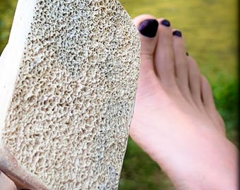 May include: A close-up of a rough, white, textured pumice stone. The stone is being held by a hand with dark nail polish.