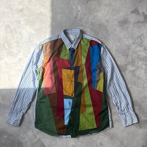 May include: A long-sleeve button-down shirt featuring a front panel composed of multi-coloured geometric fabric patches in shades of green, brown, blue, and red. The sleeves and collar are made of a light blue and white vertical pinstriped fabric.