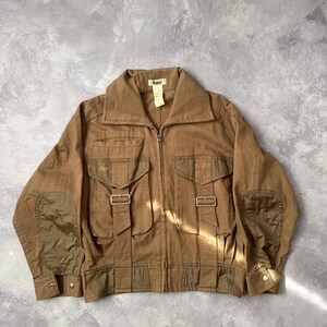 Peut inclure: Une veste utilitaire marron dotée d'une fermeture éclair frontale intégrale, d'un large col et de deux grandes poches poitrine avec fermetures à boucle. Le vêtement présente des coudières renforcées et un panneau d'ourlet inférieur contrasté.