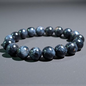 May include: A dark blue beaded bracelet. The beads are round and appear to be made of a polished stone. The bracelet is resting on a gray surface. The beads have a marbled appearance with lighter blue and white streaks.