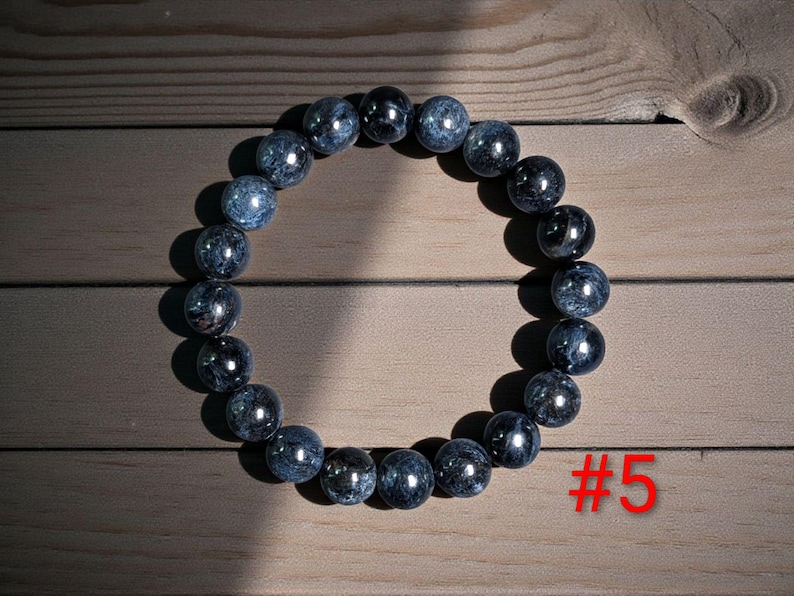 Puede incluir: Una pulsera circular compuesta por cuentas esf&eacute;ricas pulidas en tonos azul oscuro, gris y negro con una textura jaspeada. Las cuentas est&aacute;n ensartadas en un bucle continuo. El texto rojo #5 es visible en la esquina inferior derecha.
