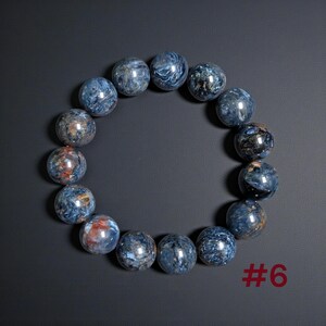 Puede incluir: Una pulsera circular compuesta por cuentas esf&eacute;ricas pulidas de piedra pietersita azul. Las cuentas presentan patrones arremolinados de azul profundo, gris y vetas ocasionales de color marr&oacute;n rojizo. El texto #6 es visible en la esquina inferior derecha.