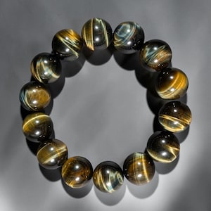 May include: A circular bracelet composed of fourteen polished, spherical tiger's eye beads. Each bead displays a chatoyant lustre with alternating bands of deep golden-brown and dark charcoal-grey, creating a shimmering, cat-eye effect throughout.