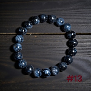 Puede incluir: Una pulsera circular de cuentas compuesta por piedras esf&eacute;ricas pulidas de color azul y negro con un patr&oacute;n arremolinado y chatoyante. Las cuentas est&aacute;n ensartadas en un bucle continuo. El texto #13 es visible en la esquina inferior derecha.