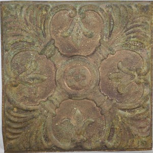 Puede incluir: Baldosa metálica cuadrada de estilo antiguo con un diseño floral en relieve. La baldosa presenta un elemento central circular rodeado de cuatro motivos florales estilizados y patrones de hojas ornamentadas. El color es una mezcla de bronce y verde.