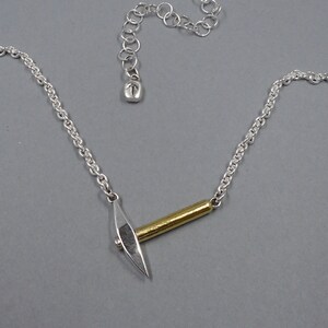May include: A silver chain necklace with a silver and gold pickaxe pendant.