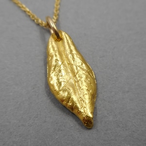 以下が含まれることがあります： 金の葉のペンダントネックレス。葉はテクスチャ加工が施され、詳細なデザインが施されています。ネックレスは繊細な金のチェーンで作られています。