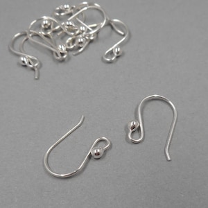 May include: Silver earring hooks with a small ball at the top. The hooks are in a pile and two are laying flat.